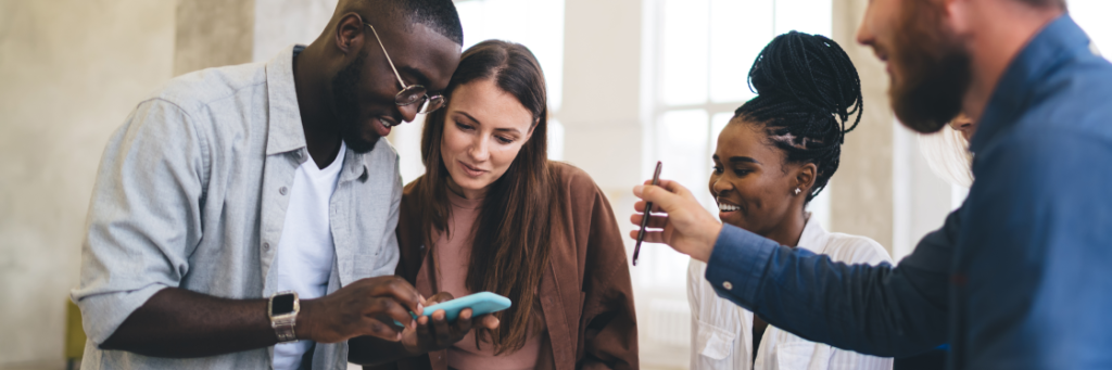 A group of four colleagues engaging with a smartphone to discuss marketing ideas during a casual meeting.