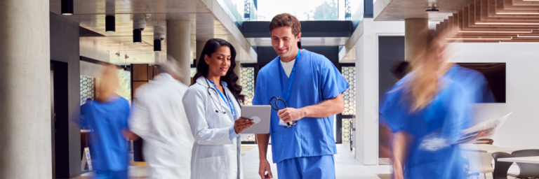 Two healthcare professionals discussing over a tablet in a busy hospital corridor.