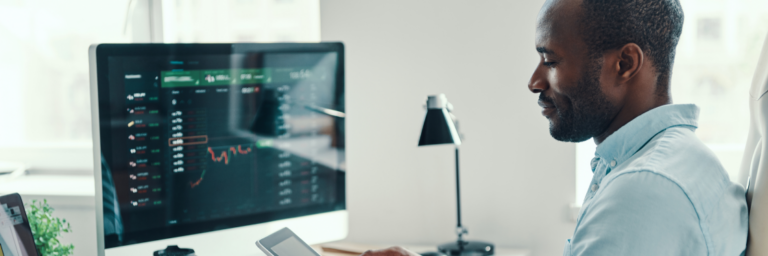 A man analyzing financial data on computer monitors in an office setting.